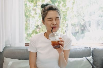 Young woman drinking milk while sitting on sofa at home