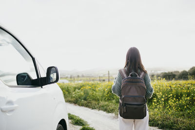 Rear view of woman with backpack looking at field standing by van against sky
