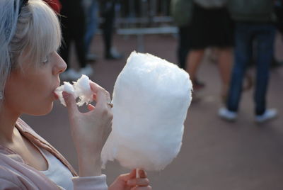 Young woman eating cotton candy while standing on street