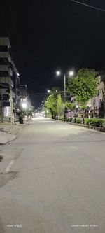 Empty road by illuminated buildings in city at night