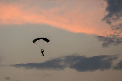 Low angle view of person paragliding against sky during sunset