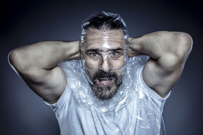 Portrait of man covering face with plastic against gray background