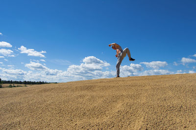 Low angle view of man posing on landscape against blue sky
