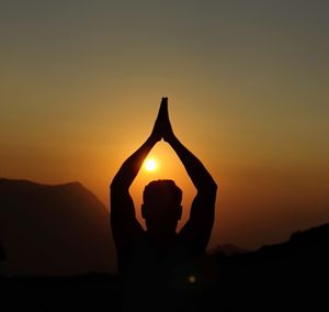 Cropped hand of man holding heart shape against sky during sunset