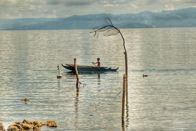 Man sitting in boat on lake against sky