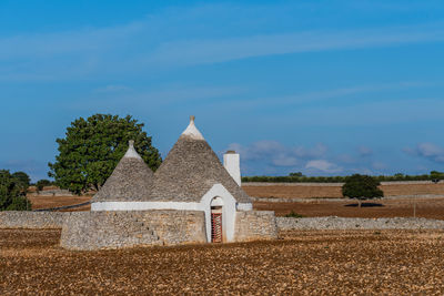 Trulli houses on field by trees against sky