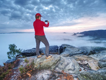Rear view of man standing on rock against sky
