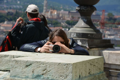 Young woman holding camera while standing on table