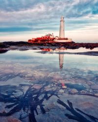 Lighthouse by sea against sky during sunset