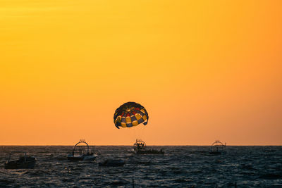 Silhouette man with parachute against sky during sunset