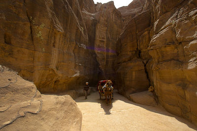 Man walking by horse cart on dirt road between rock formations during sunny day