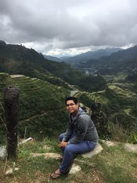 Portrait of young man sitting on landscape against sky