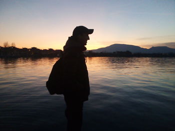 Silhouette man standing by lake against sky during sunset