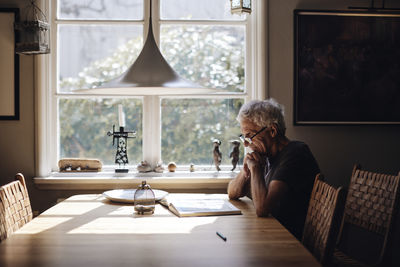 Senior man with eyeglasses reading book on table at home