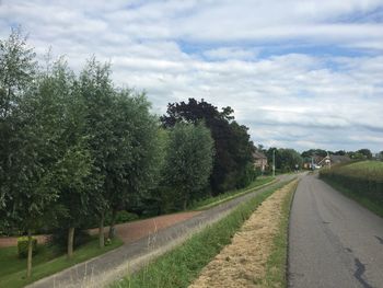 Empty road amidst trees on field against sky