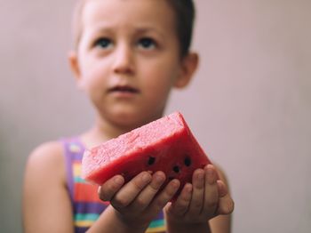 Boy holding slice of watermelon against wall