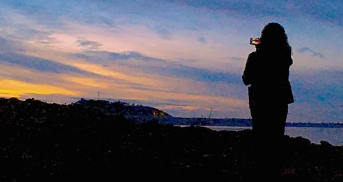 Silhouette of woman standing on landscape against sunset sky