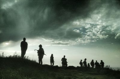 Silhouette people standing on grass against sky