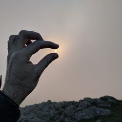 Midsection of man holding rock against sky during sunset