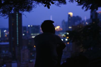 Rear view of silhouette man against illuminated cityscape at night