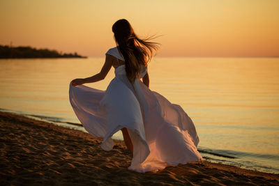 Young woman runs in a white dress on the seashore at sunset