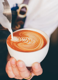 Midsection of barista pouring cream in coffee at cafe