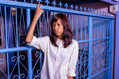 Portrait of young woman standing by fence