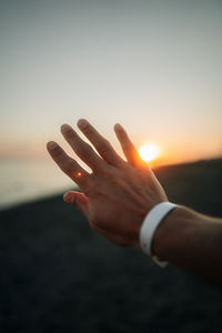 Cropped hand of person against sky during sunset