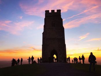 People at historical building against sky during sunset