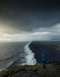 Rear view of man standing on sea shore against sky