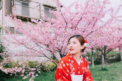 Woman standing against pink cherry blossom tree