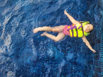 A cute asian girl wearing a pink swimsuit and a green life jacket is playing in the swimming pool.