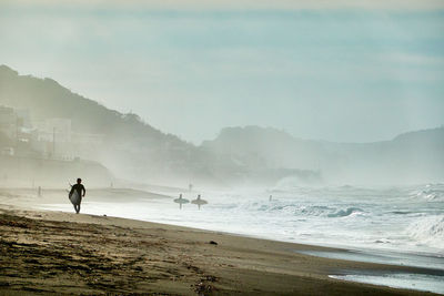 People on beach against sky during foggy morning