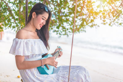 Young woman playing guitar while sitting at beach