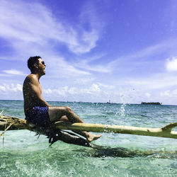 Side view of shirtless man in sea against sky