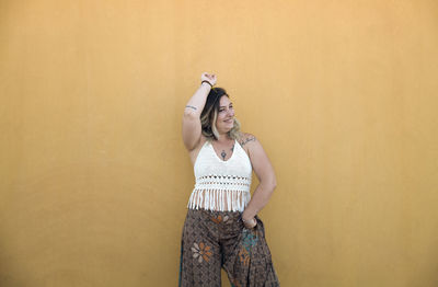 Portrait of smiling young woman dancing against yellow wall in summer