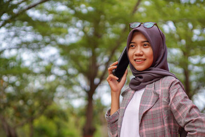 Portrait of young woman standing against trees