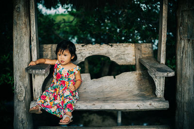 Baby girl looking away while sitting on wooden bench at park