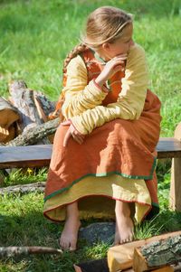 Woman in traditional clothes sitting on bench at field