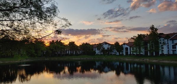 Scenic view of lake by silhouette trees and buildings against sky