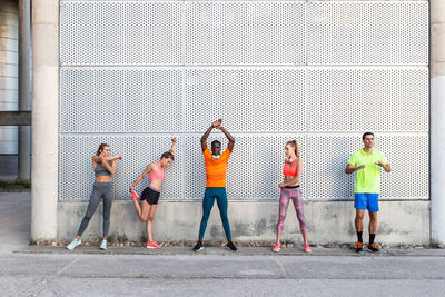 Group of multiracial runners in activewear standing in street and stretching muscles while preparing for training in city