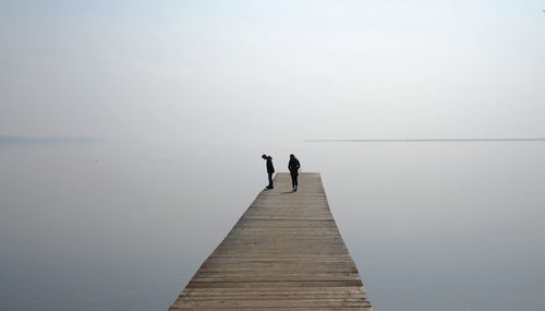 People on pier over sea against clear sky