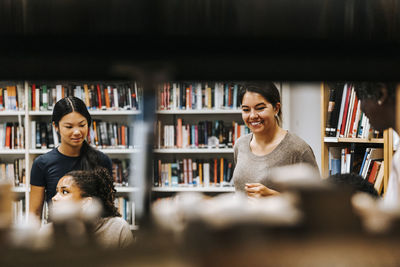 Happy female librarian with students in library at school