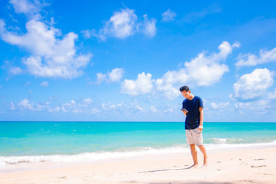 Young man using phone while walking on sand at beach