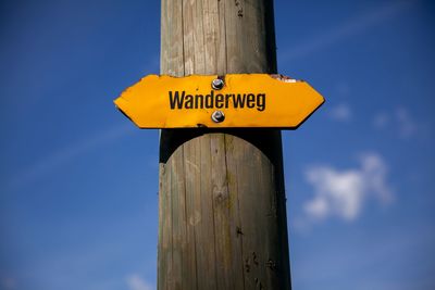 Low angle view of information sign on wooden post against blue sky