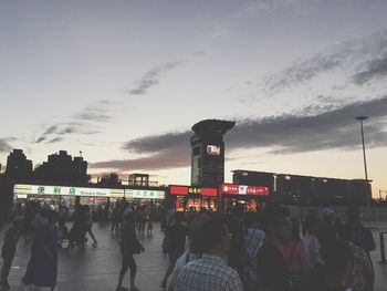 People walking on illuminated city against sky