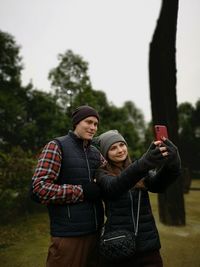 Young woman taking selfie with partner through mobile phone while standing in park