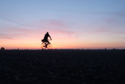 Silhouette man riding bicycle on road against sky during sunset