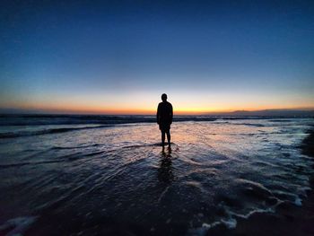 Silhouette man standing on beach against sky during sunset