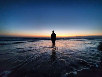 Silhouette man standing at beach against sky during sunset